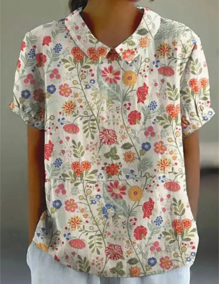 Camicia donna a maniche corte con stampa floreale colorata, colletto classico, sfondo bianco. Moda estiva casual, tessuto leggero.