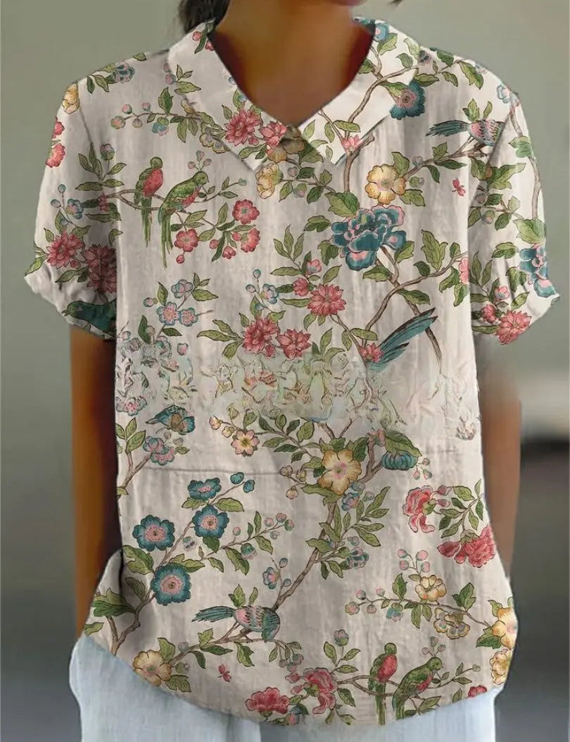 Camicia donna a maniche corte con stampa floreale e uccelli, colletto classico, sfondo bianco, stile casual estivo, tessuto leggero e traspirante.