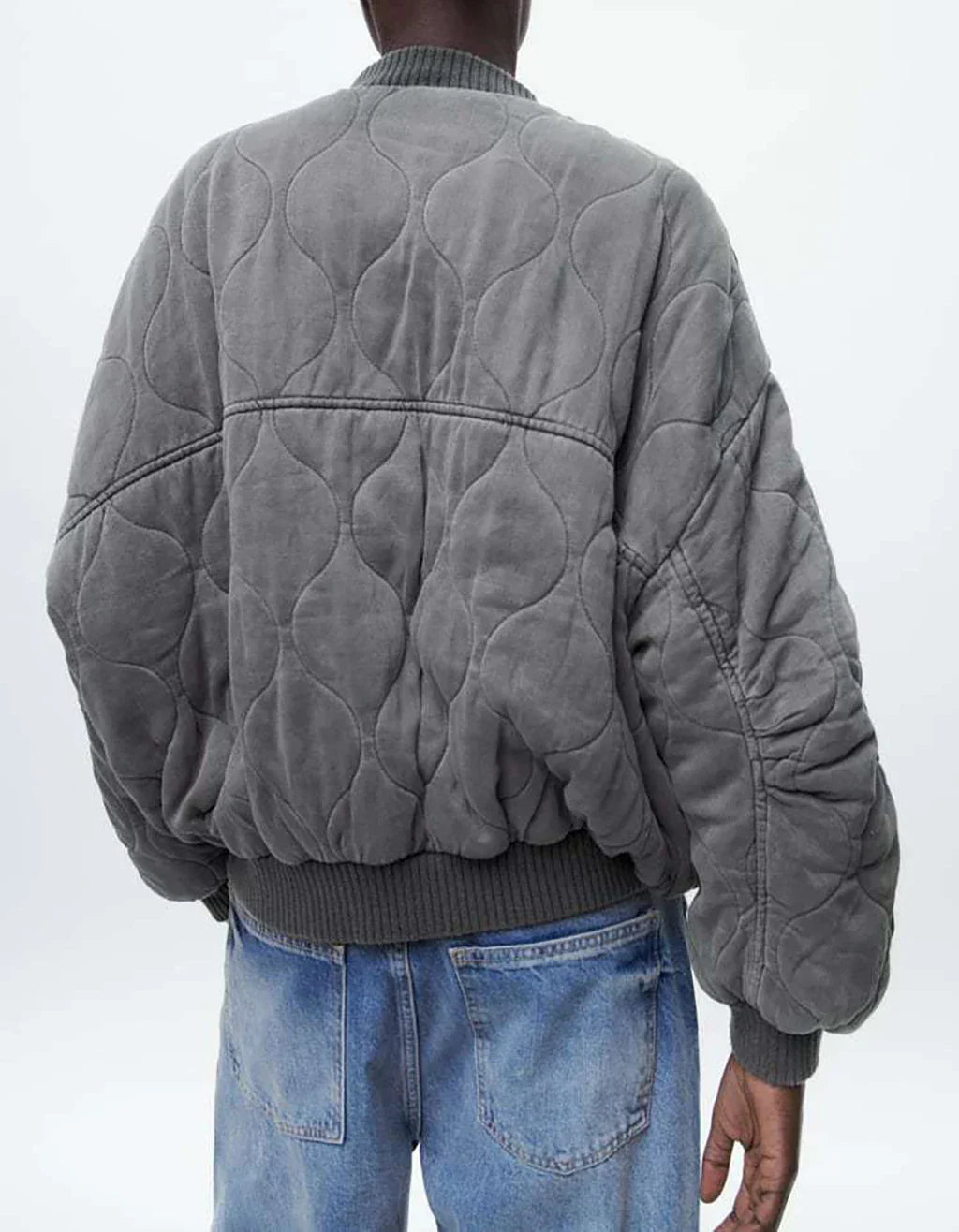 Giacca bomber grigia trapuntata, design oversize, indossata da uomo, abbinata a jeans blu. Moda casual, stile urbano, tendenza autunno inverno.