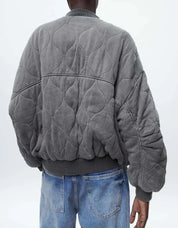Giacca bomber grigia trapuntata, design oversize, indossata da uomo, abbinata a jeans blu. Moda casual, stile urbano, tendenza autunno inverno.