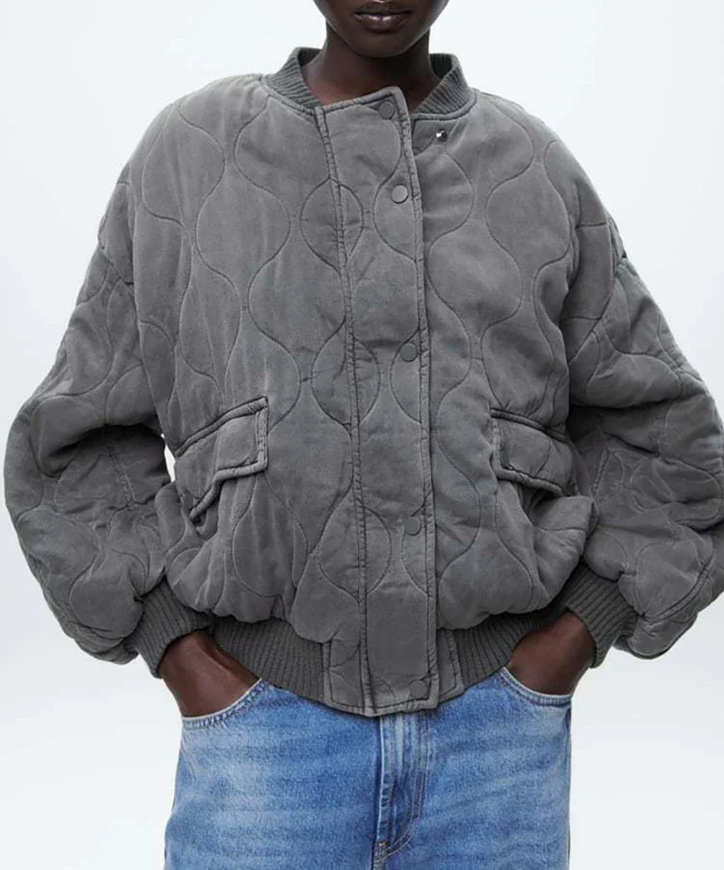 Giacca bomber trapuntata grigia, stile casual, con tasche frontali e polsini a coste, indossata con jeans blu. Moda autunno inverno donna.