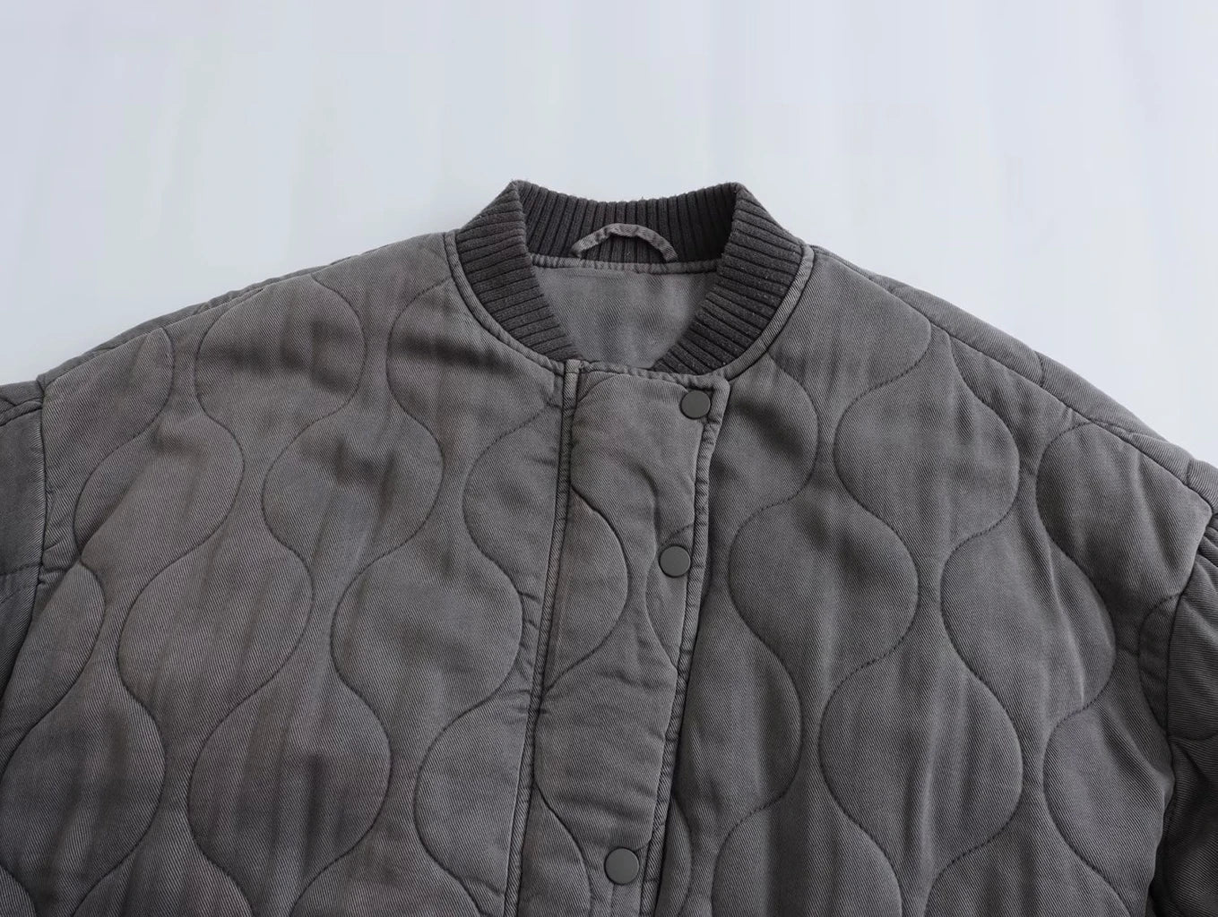 Giacca trapuntata grigia con bottoni a pressione, colletto a coste, design ondulato. Moda autunnale, abbigliamento casual, stile moderno.