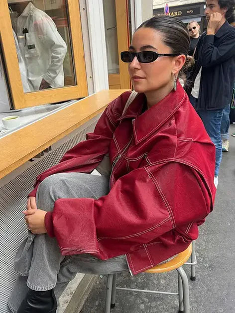 Donna con giacca oversize rossa, occhiali da sole neri, seduta all'aperto. Moda urbana, stile casual, abbigliamento autunnale.
