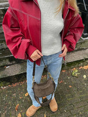 Giacca rossa in pelle, maglione grigio, jeans blu, borsa marrone scamosciata, stivali beige. Moda autunnale casual donna, stile urbano.