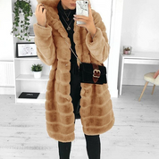 Cappotto lungo in pelliccia sintetica beige, donna, elegante, con borsa nera a tracolla. Outfit invernale alla moda, interno casa minimalista.