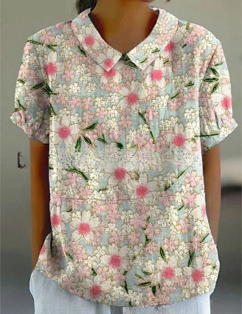Camicia donna a maniche corte con colletto, fantasia floreale rosa e bianca su sfondo azzurro, stile casual estivo.