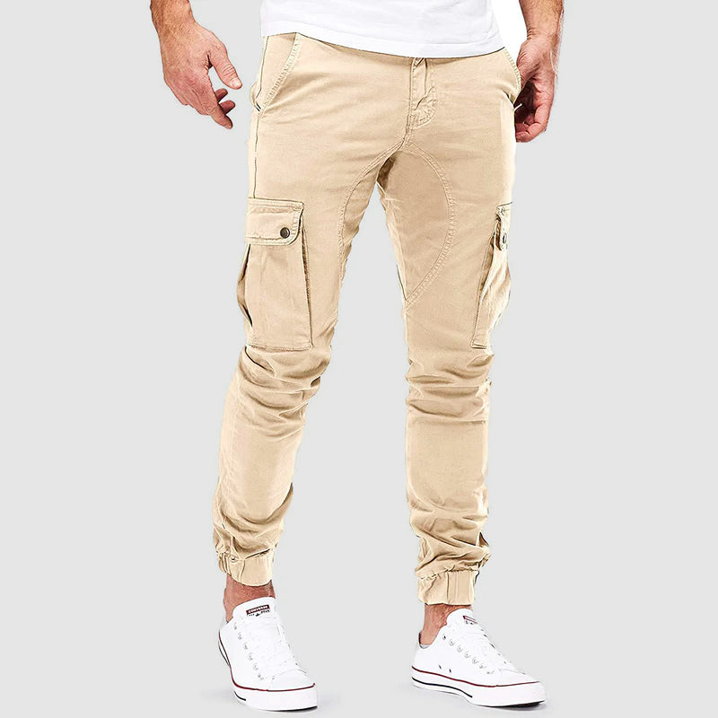Pantaloni cargo beige da uomo, tasche laterali, vestibilità slim, abbinati a scarpe da ginnastica bianche. Stile casual moderno.