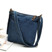 Borsa a tracolla in denim blu con cuciture a contrasto, chiusura a zip e dettagli in pelle marrone. Accessorio moda casual per donna.