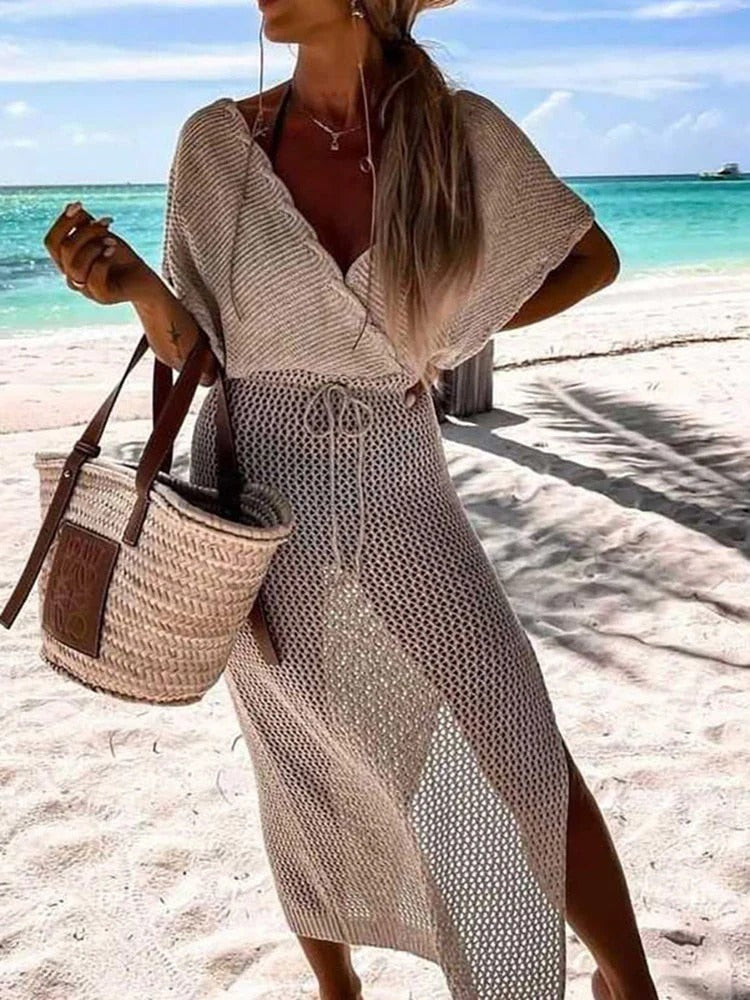 Donna in spiaggia con abito crochet beige, borsa di paglia, mare turchese sullo sfondo. Moda estiva, abbigliamento da spiaggia elegante.