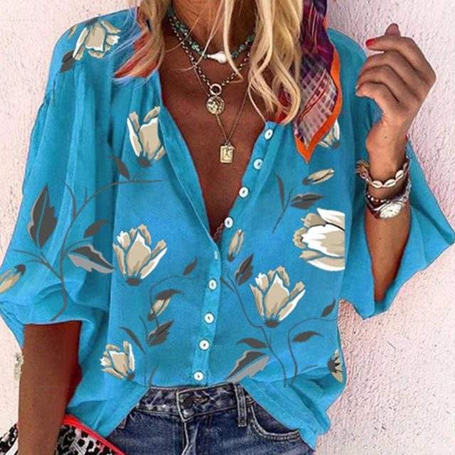 Camicia donna blu con stampa floreale, maniche corte, abbottonatura frontale, abbinata a collane e bracciali. Moda estiva casual elegante.