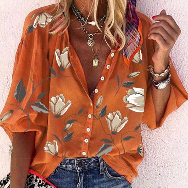 Camicia donna arancione con stampa floreale, maniche corte, abbottonatura frontale, abbinata a jeans. Accessori: collane, bracciali, foulard colorato.