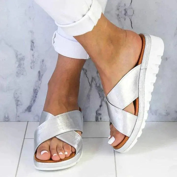 Sandali donna argento con suola bianca, design incrociato, indossati su pavimento bianco. Scarpe estive eleganti e comode.