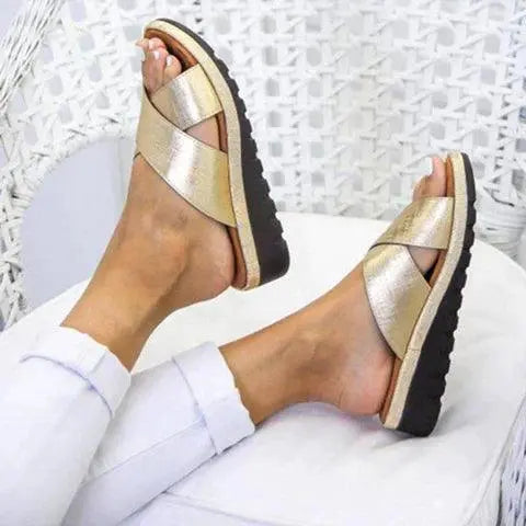 Sandali donna dorati con suola nera, design incrociato, indossati su gambe con jeans bianchi. Calzature estive eleganti e comode.
