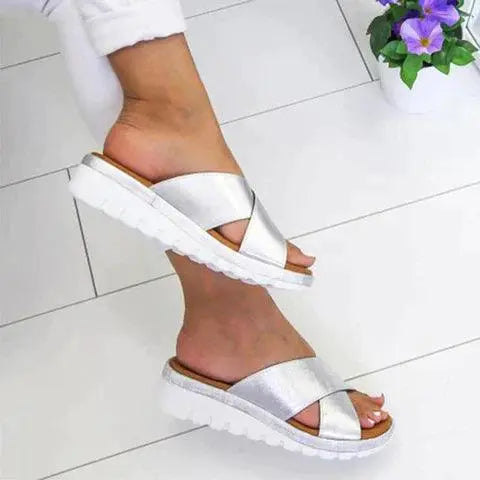 Sandali donna argento con suola bianca, design incrociato, indossati su pavimento bianco. Scarpe estive eleganti e comode.