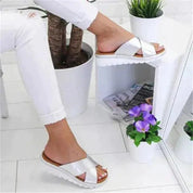 Sandali donna argento con suola bianca, indossati con pantaloni bianchi. Design incrociato, stile estivo, moda casual.