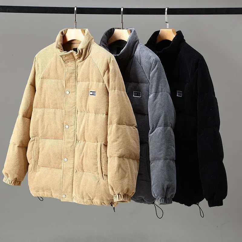 Giacca invernale trapuntata in velluto a coste, disponibile in beige, grigio e nero, appesa su gruccia. Moda uomo, abbigliamento caldo, casual.