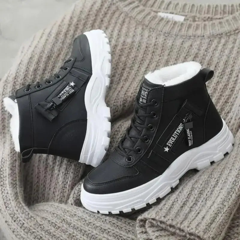 Scarponcini neri invernali da donna con suola bianca, dettagli in pelliccia sintetica, su maglione beige. Scarpe moda calde e resistenti.