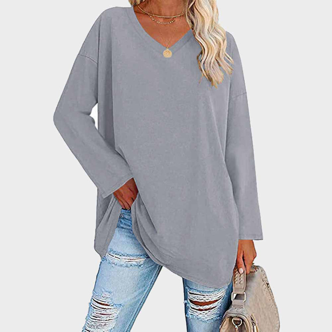 Maglia oversize grigia donna, scollo a V, maniche lunghe, abbinata a jeans strappati e borsa beige. Moda casual autunnale.