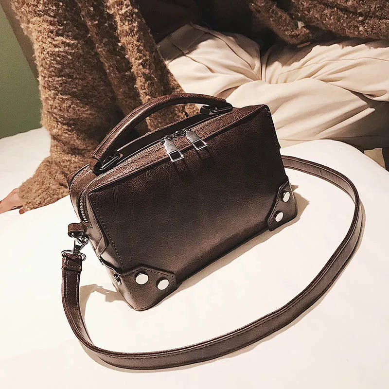 Borsa a tracolla in pelle marrone su letto, design elegante con manico superiore e dettagli metallici, perfetta per moda autunno inverno.