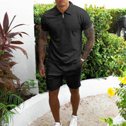Uomo in abbigliamento casual estivo, indossa polo nera e pantaloncini, circondato da piante verdi. Look moderno e rilassato per l'estate.