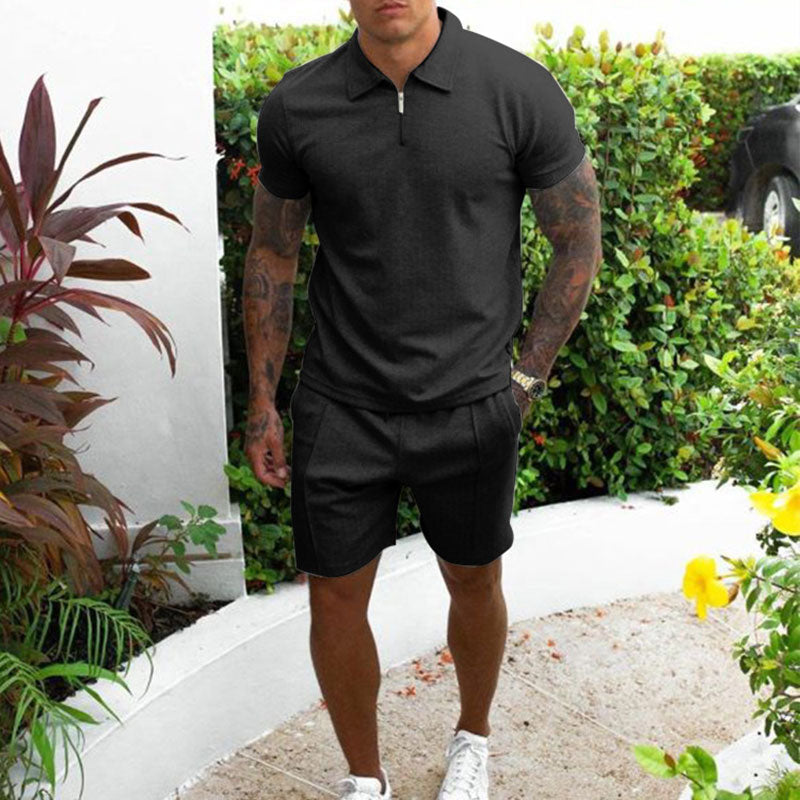 Uomo in abbigliamento casual estivo, indossa polo nera e pantaloncini, circondato da piante verdi. Look moderno e rilassato per l'estate.