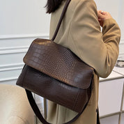 Borsa a tracolla in pelle marrone con motivo coccodrillo, indossata su cappotto beige. Elegante accessorio moda donna, perfetto per l'autunno.