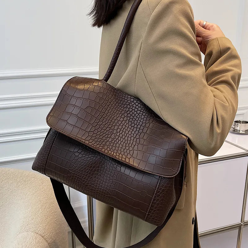 Borsa a tracolla in pelle marrone con motivo coccodrillo, indossata su cappotto beige. Elegante accessorio moda donna, perfetto per l'autunno.