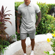 Uomo in completo estivo grigio, polo e pantaloncini, in giardino. Look casual elegante, moda maschile, abbigliamento estivo, scarpe bianche.