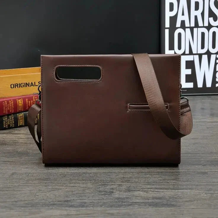 Borsa a tracolla in pelle marrone scuro, design elegante e moderno, con manico integrato e cinturino regolabile, su sfondo di libri e poster.