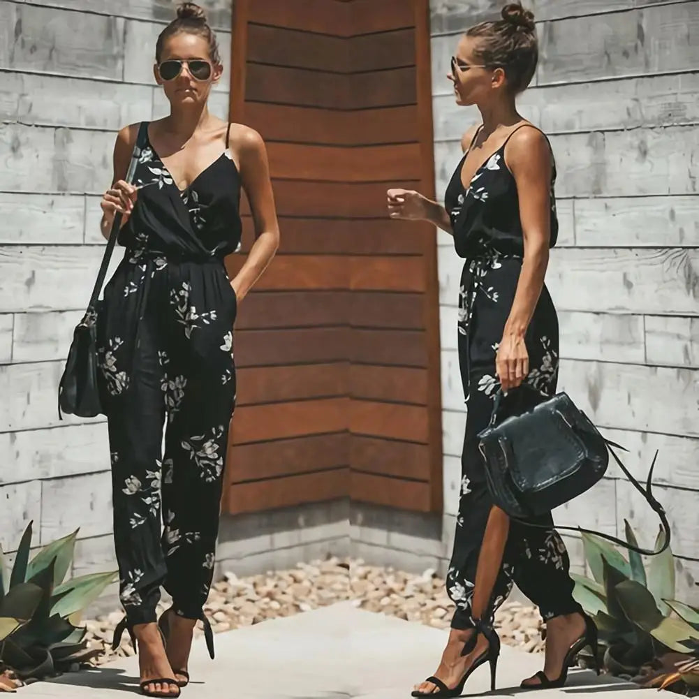 Donna con tuta nera floreale, sandali con tacco e borsa a tracolla. Moda estiva elegante, look casual chic. Sfondo in legno e piante.