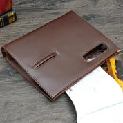 Custodia in pelle marrone per tablet su tavolo in legno, design elegante con aperture per accesso facile. Accessorio tecnologico di alta qualità.