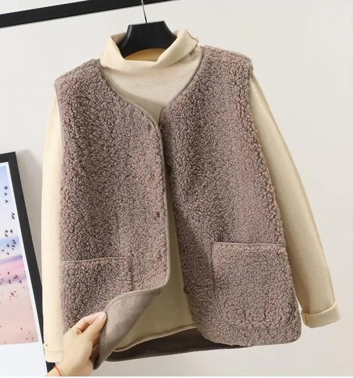 Gilet in pile marrone su maglione beige, appeso su gruccia. Moda autunno inverno, abbigliamento casual donna, tessuto caldo e morbido.