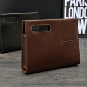 Elegante borsa a mano in pelle marrone su tavolo di legno, design moderno con manico integrato. Sfondo nero con scritta parziale.