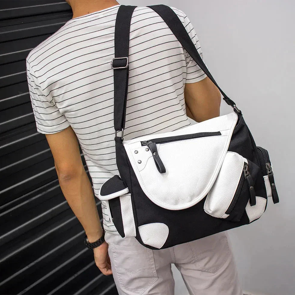 Borsa a tracolla unisex bianca e nera, design moderno, tasche multiple, indossata da persona con maglietta a righe. Accessorio moda casual.