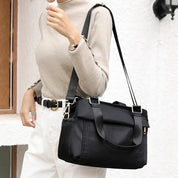 Donna con borsa a tracolla nera in tessuto, indossa maglione beige e pantaloni bianchi. Accessorio moda elegante e pratico per uso quotidiano.