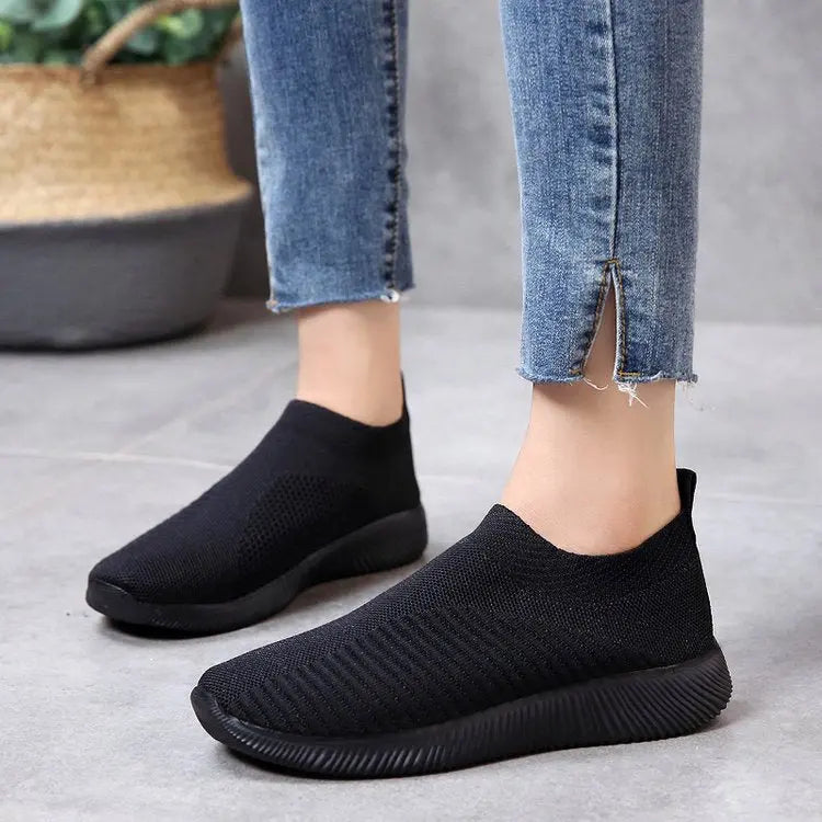 Scarpe da ginnastica nere senza lacci, design moderno e traspirante, indossate con jeans. Scarpe casual unisex, comode per uso quotidiano.