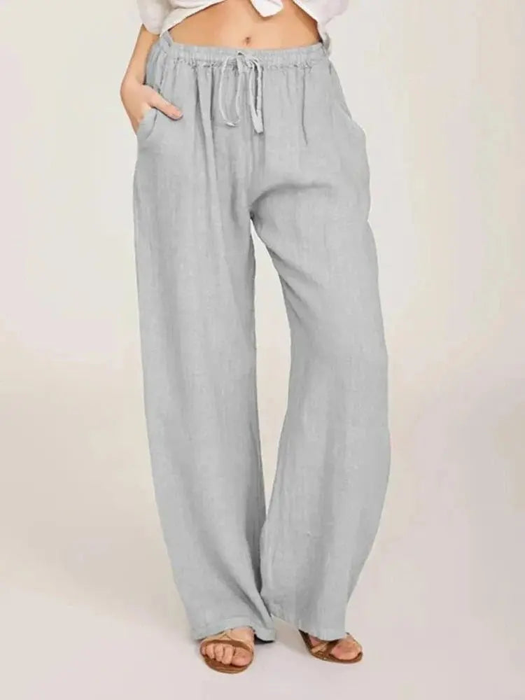 Pantaloni larghi in lino grigio chiaro da donna, con tasche e coulisse in vita, stile casual estivo. Indossati con sandali marroni.