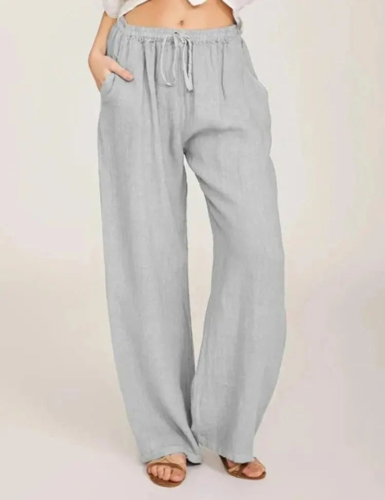 Pantaloni larghi in lino grigio chiaro da donna, con tasche e coulisse in vita, stile casual estivo. Indossati con sandali marroni.