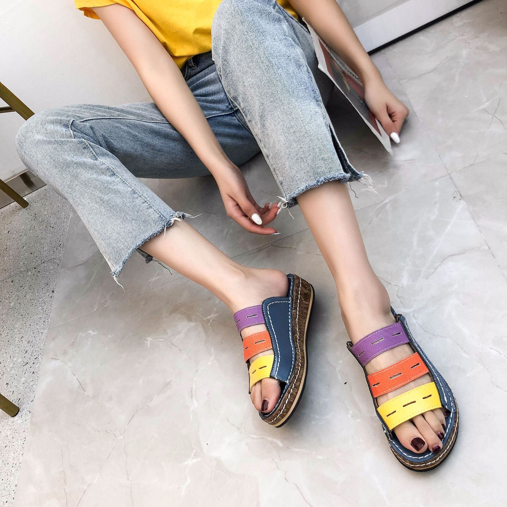 Sandali colorati da donna con fasce multicolore su pavimento in marmo. Moda estiva, calzature casual, jeans chiari, top giallo.
