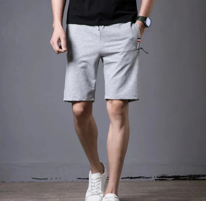 Pantaloncini uomo grigi casual, tasche laterali, indossati con t-shirt nera e scarpe bianche. Stile estivo, moda maschile, abbigliamento comodo.