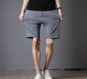 Pantaloncini sportivi grigi da uomo, elastici, con tasche, indossati con scarpe bianche. Ideali per fitness e tempo libero.