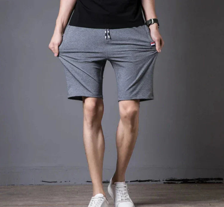 Pantaloncini sportivi grigi da uomo, elastici, con tasche, indossati con scarpe bianche. Ideali per fitness e tempo libero.