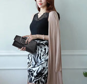 Donna elegante con abito nero e bianco a fantasia, cardigan beige, borsa nera con manico metallico. Moda femminile, abbigliamento chic.