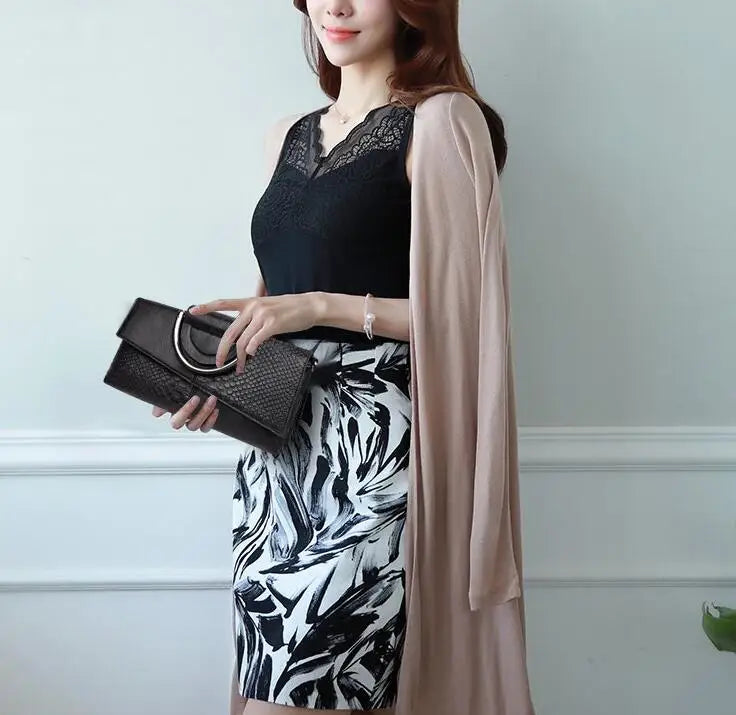 Donna elegante con abito nero e bianco a fantasia, cardigan beige, borsa nera con manico metallico. Moda femminile, abbigliamento chic.