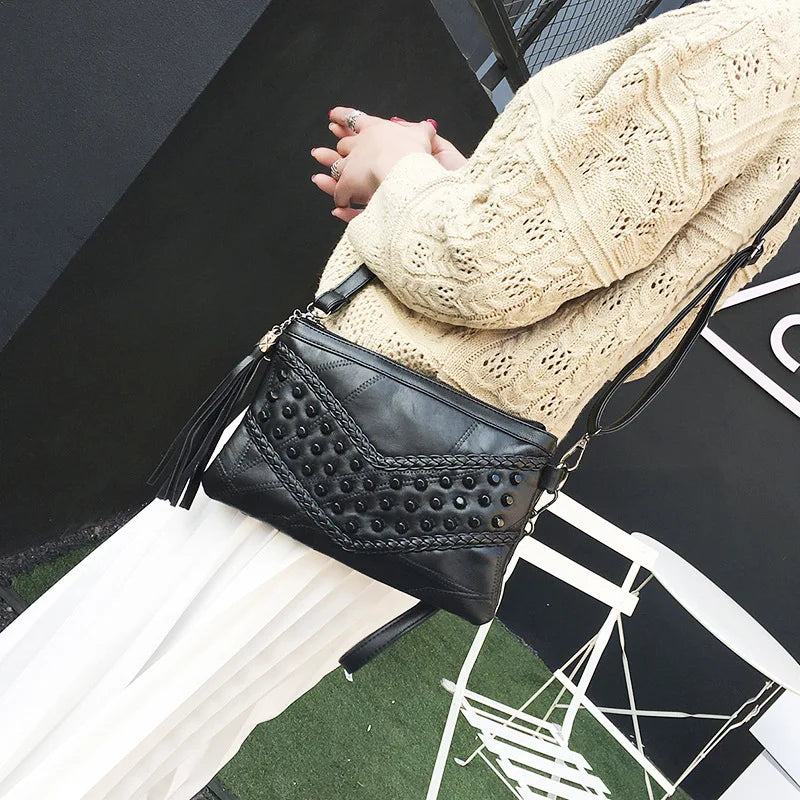 Borsa a tracolla nera in pelle con borchie, indossata da una donna in maglione beige. Accessorio moda elegante per donna.