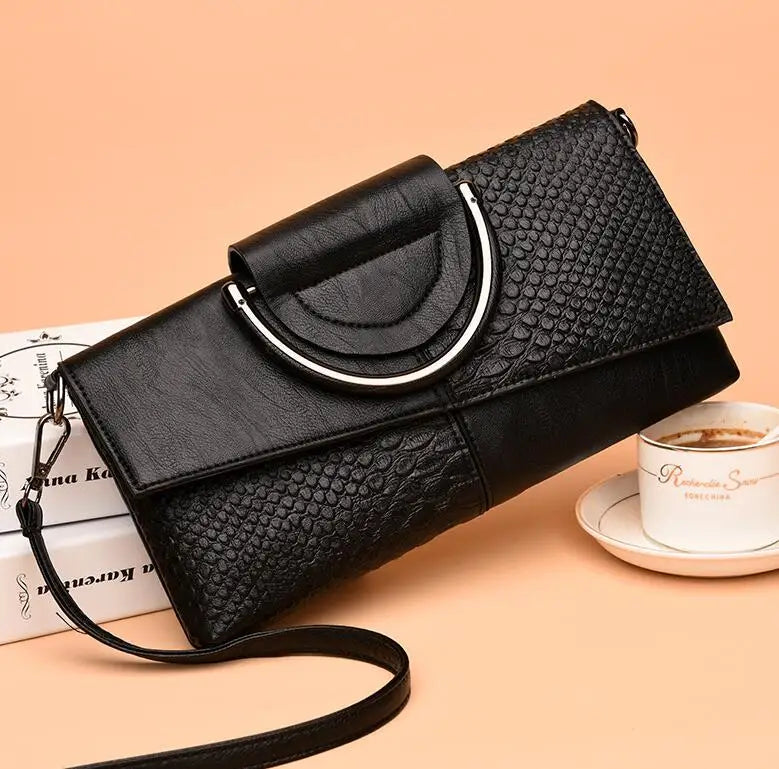 Elegante borsa a tracolla nera in pelle con texture a serpente, chiusura metallica, su sfondo beige. Accessorio moda donna, stile sofisticato.