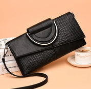 Elegante borsa a tracolla nera in pelle con texture a serpente, chiusura metallica, su sfondo beige. Accessorio moda donna, stile sofisticato.