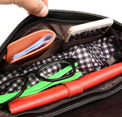 Interno di una borsa nera con occhiali, portafoglio arancione, smartphone e quaderno rosso su fodera a quadri. Accessori moda, organizzazione borsa.