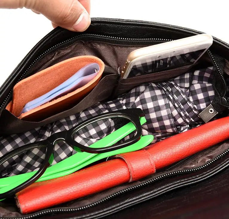 Interno di una borsa nera con occhiali, portafoglio arancione, smartphone e quaderno rosso su fodera a quadri. Accessori moda, organizzazione borsa.