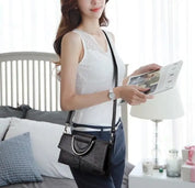 Donna con borsa a tracolla nera in pelle, design elegante, indossa top bianco e pantaloni blu, in una stanza moderna. Accessorio moda femminile.
